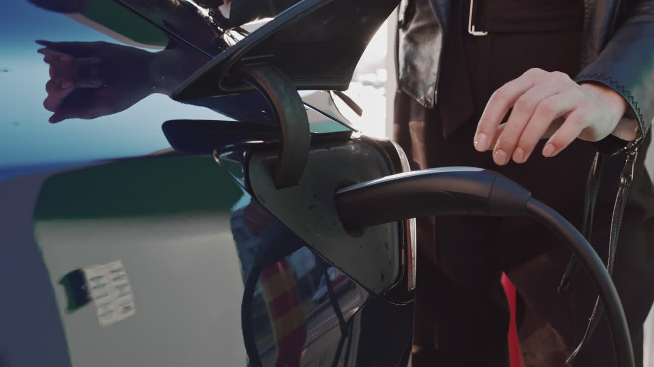 Ładowanie samochodu elektrycznego w zwolnionym tempie – kobieca dłoń dotyka wtyczki stacji ładującej