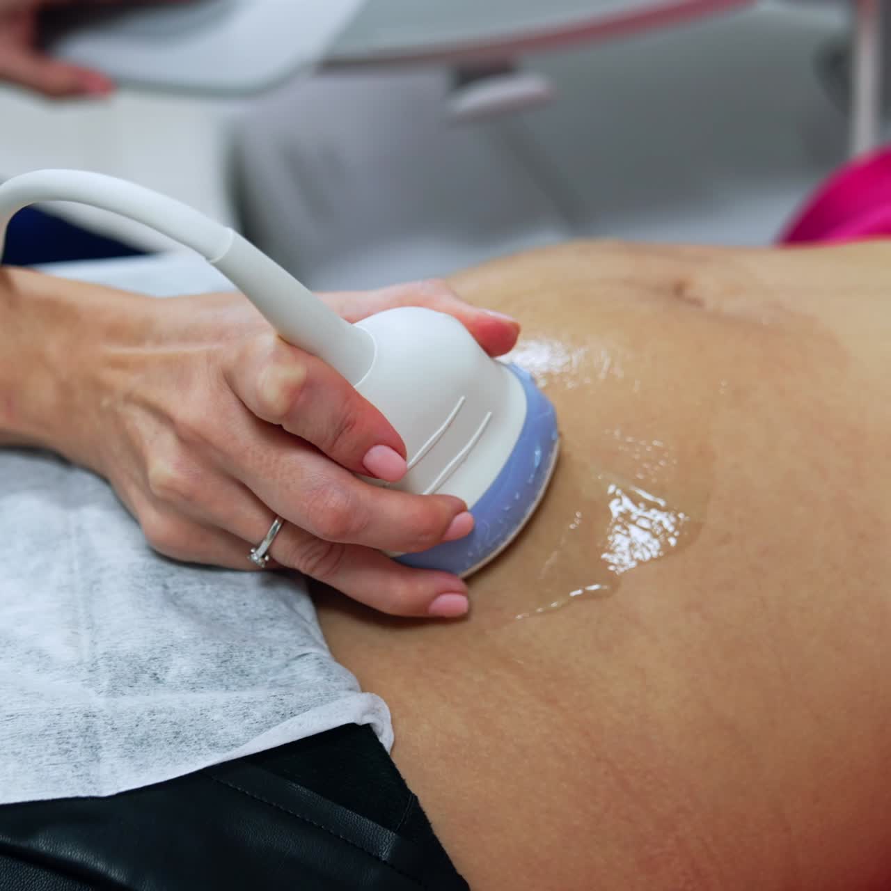 Pregnant belly of a woman on the early stages of pregnancy. Doctor's hand uses device to check the baby on the ultrasound machine