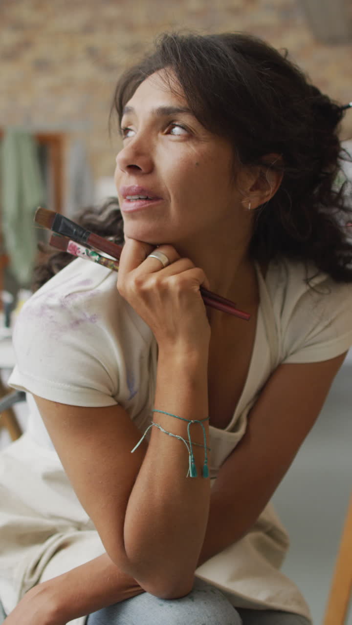 video vertical de una artista biracial pensativa sentada en el estudio