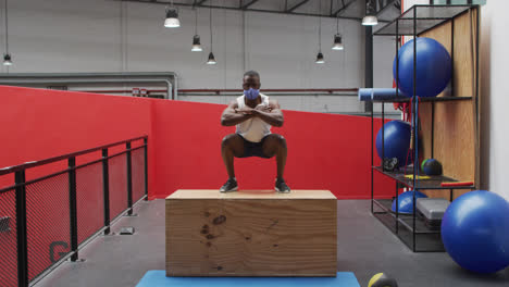 Afroamerikanischer-Mann-Springt-Mit-Gesichtsmaske-Im-Fitnessstudio-Auf-Eine-Kiste