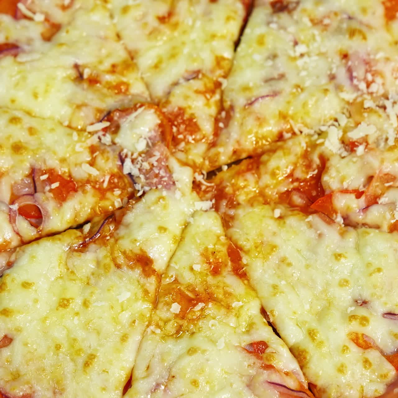 Ready pizza is sprinkling with cheese. Well baked pizza with melted cheese and other ingredients. Tasty snack. Close-up. Top view