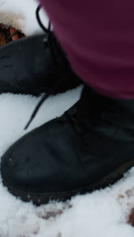 primer plano de una bota negra saltando en el suelo helado, dejando una huella de zapato distinta en la nieve fresca, hojas secas esparcidas añaden textura al paisaje congelado