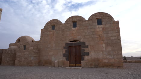 wide pan shot of unesco world heritage site qasr amra desert castle with three domes on a cloudy day