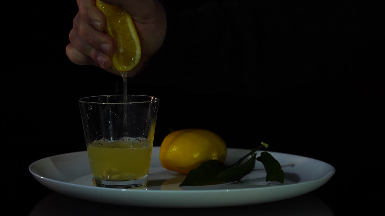 Mano exprimiendo limón amarillo en rodajas en un vaso, zumo fresco de cítricos con vitaminas.