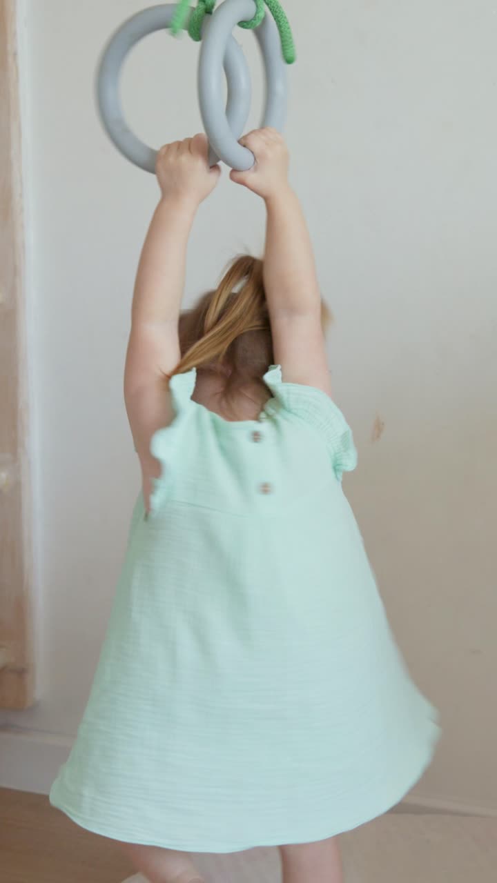 Bambina che gioca e si dondola agli anelli da ginnastica in casa