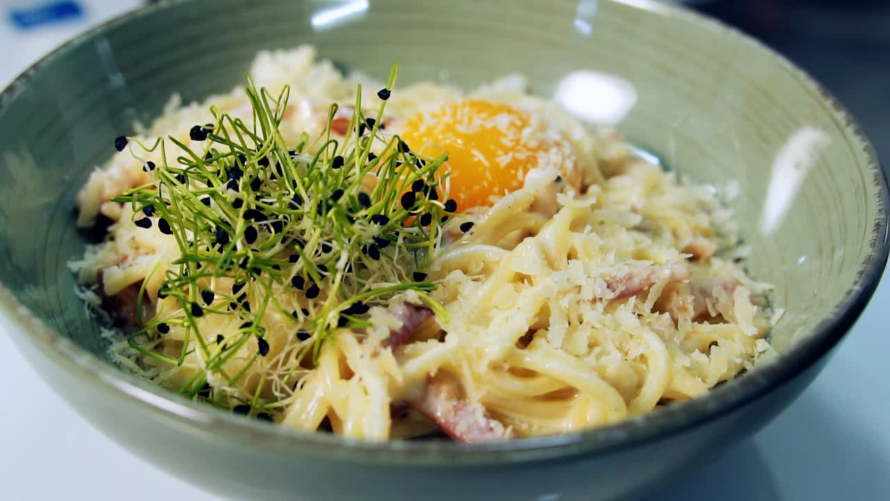 Delicious meal in a plate spinning. Tasty cooked pasta with yolk and green sprouts in the restaurant. Close-up. Pleasant appetite