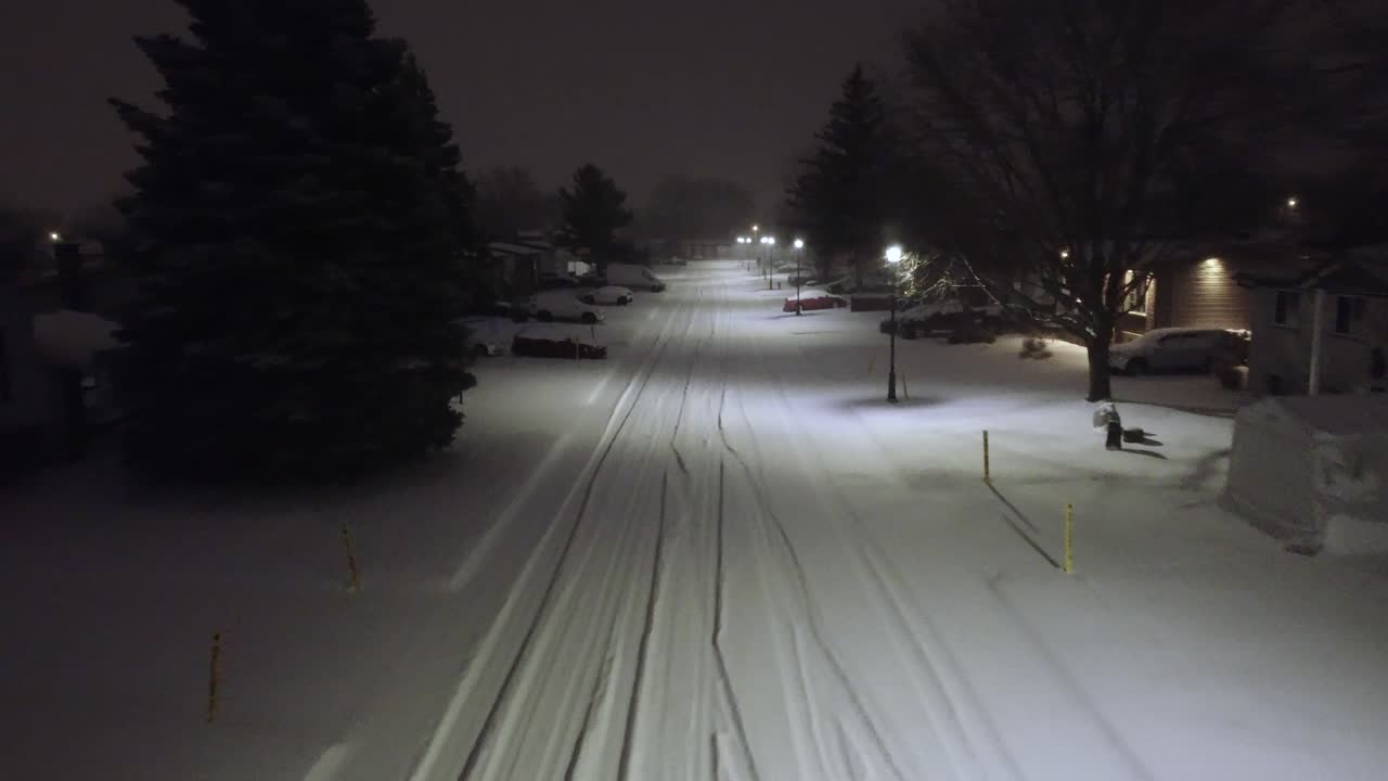 Travelling up a quiet street at night illuminated by streetlights in a snow shower