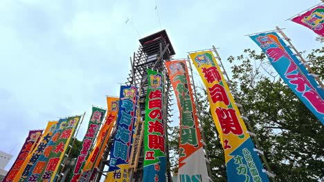 vibrant, colorful flags (nobori) celebrating sumo wrestlers stand tall against the sky near a traditional tower, indicating a festive sumo atmosphere.