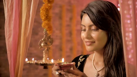 a good looking female in a sari lights the hanging oil lamp and smiles looking into the camera