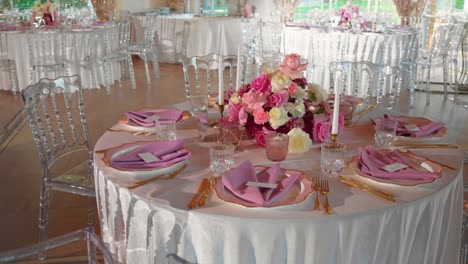 shot of fancy wedding reception tables with glasses and plates, table is decorated with gorgeous pink and white roses and white candles, rotating shot