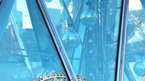 Noria-Gigante-Reflejada-En-Un-Edificio-De-Cristal-Bajo-Un-Cielo-Azul-Claro,-Arquitectura,-Atracción-De-Feria