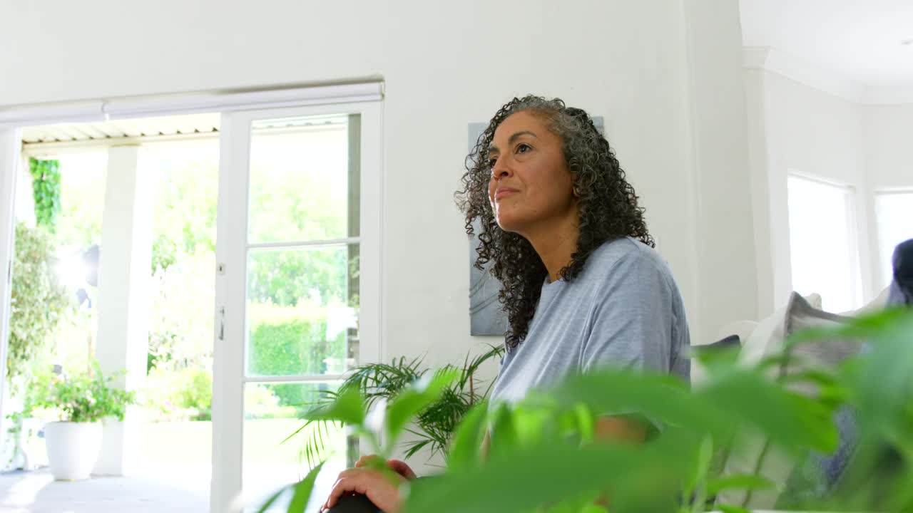 Donna seduta sul divano vicino a una porta scorrevole, la telecamera si avvicina, chiude gli occhi pensando, spazio per il testo.