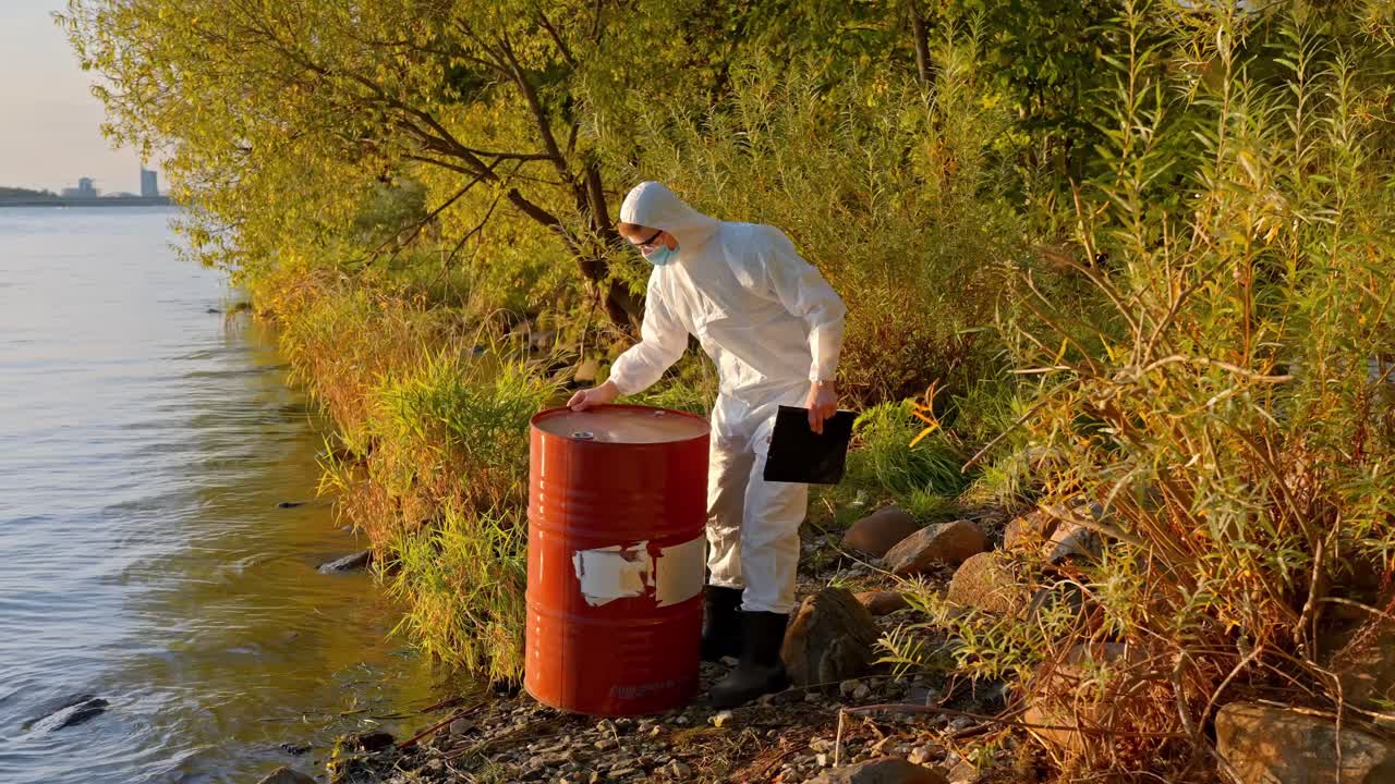 Scientist in hazmat suit takes notes beside oil drum during environmental site check