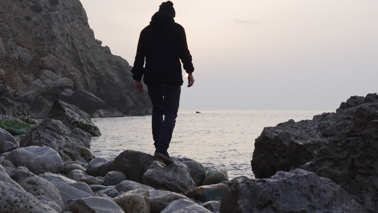 el hombre sube a una roca al lado del mar para presenciar el amanecer en una mañana gris brumosa