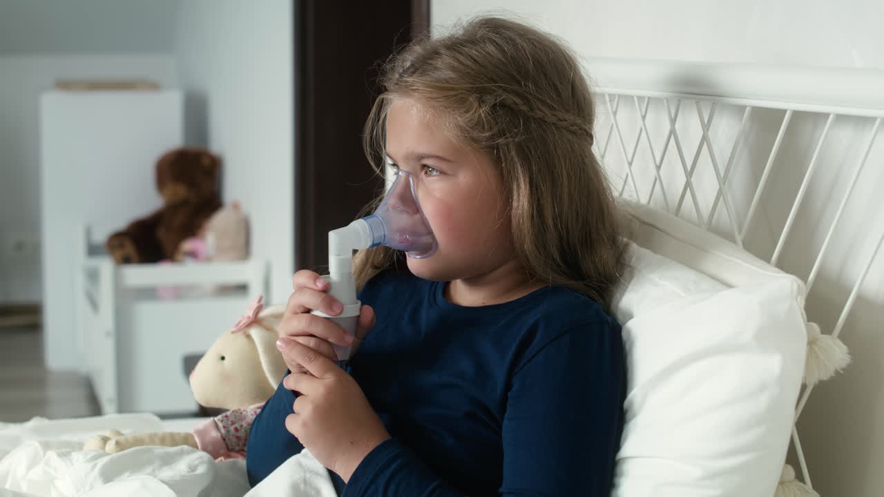 niña de edad primaria usando nebulizador en la cama en casa.