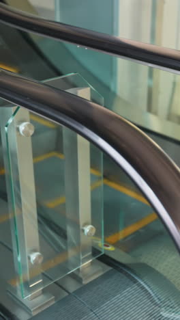 perspectiva en primera persona que muestra una vista cercana de dos escaleras mecánicas, una subiendo y la otra bajando. las barandillas y escalones de la escalera mecánica en un entorno interior moderno