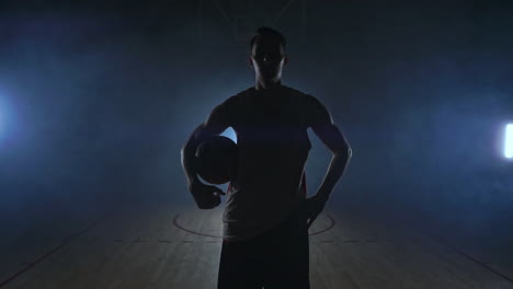 Der-Basketballspieler-Geht-Zur-Kamera-Und-Wirft-Den-Ball-Auf-Den-Boden.-Dann-Bleibt-Er-Stehen,-Hält-Den-Ball-Und-Blickt-In-Die-Kamera