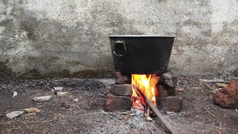 a traditional food pot on a chulha in an open space in maharashtra, india. flames from burning wood heat the vessel, creating a rustic cooking scene rooted in rural indian culture and simplicity