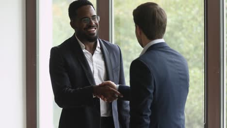 happy biracial manager in eyewear shaking hands with motivated partner.