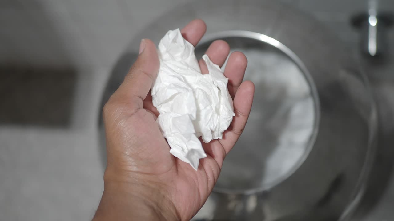 Hand holding tissue over a waste bin