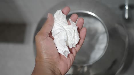 hand holding tissue over a waste bin