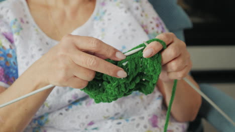 elderly woman knitting a green sweater