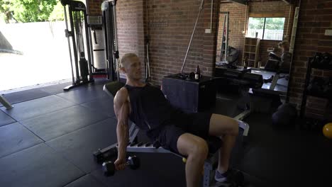 músculos de hombre tatuado en el gimnasio en casa haciendo flexiones de bíceps sentados