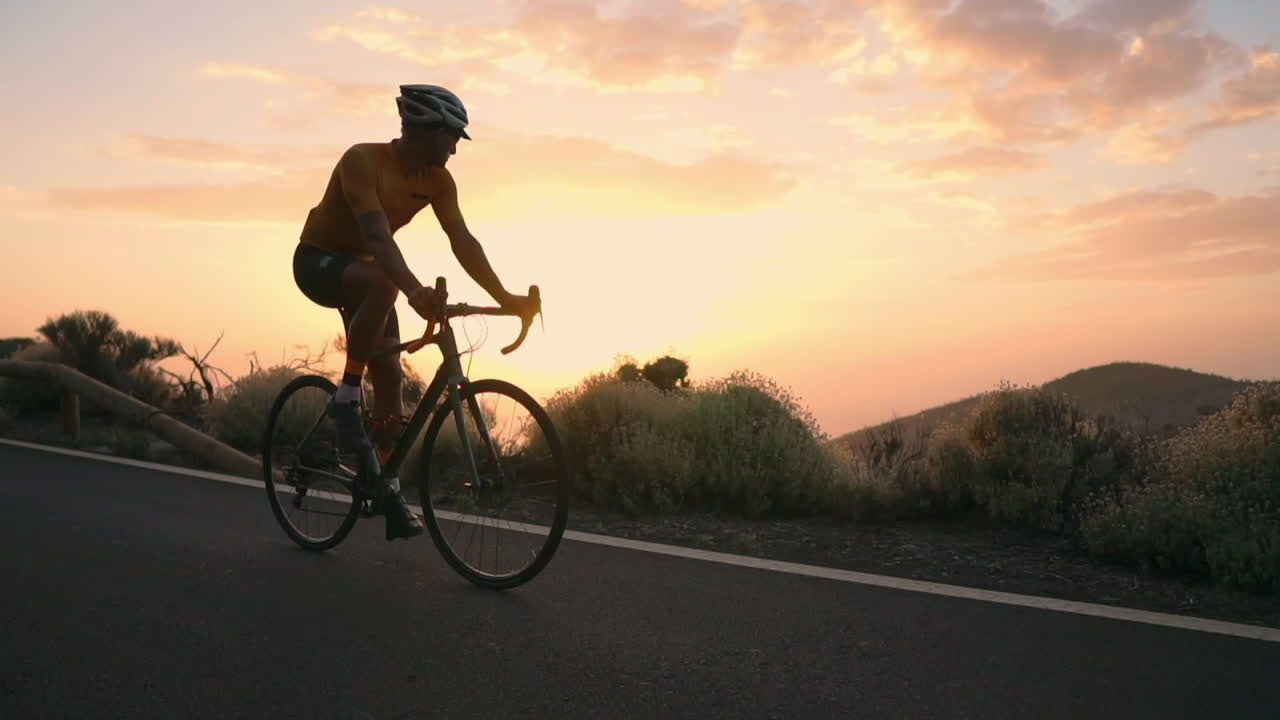 The athlete on a bike is seen in slow motion conquering a mountain serpentine, cherishing the island's view, epitomizing a devotion to a healthy lifestyle at sunset
