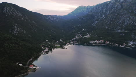 a coastal town on the shores of the bay of kotor in montenegro, surrounded by high mountains covered with vegetation,light morning glow above the peaks, buildings and trees on the mountainside,aerial