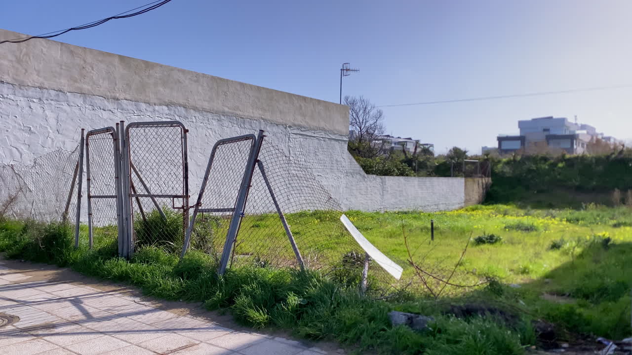Verlassener Maschendrahtzaun versperrt den Zugang zu einem wilden grünen Feld mit gelben Wildblumen in der Landschaft von Sanlúcar de Barrameda