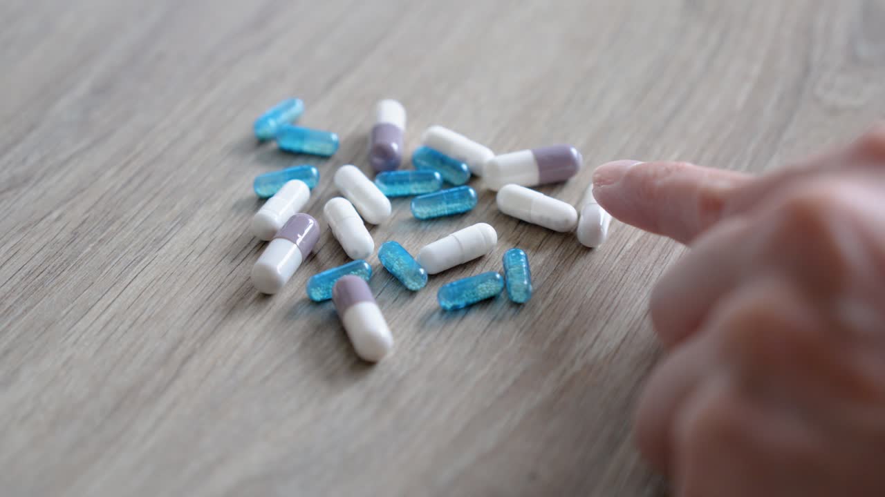 colorful pills on table with hand selecting one capsule