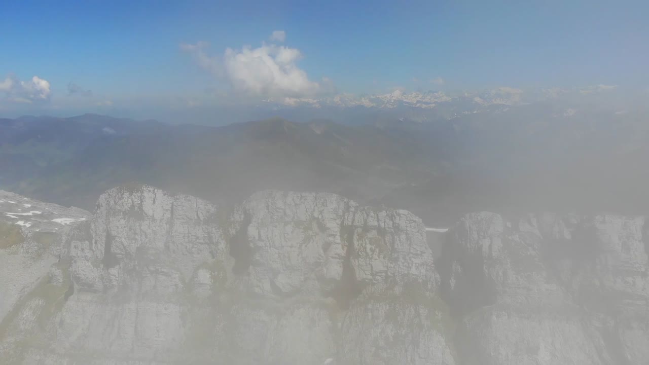 Drone footage captures majestic rocky mountains in Switzerland, shrouded in cloudy weather, creating dramatic and atmospheric view of rugged alpine landscape