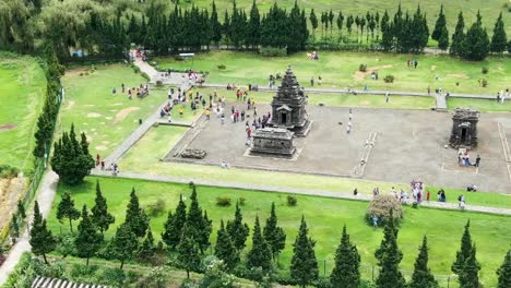 Ancient-temple-in-Indonesia-with-many-tourists,-aerial-orbit-view