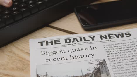 newspaper headline featuring devastation caused by earthquake disaster on desk next to computer keyboard and phone 1