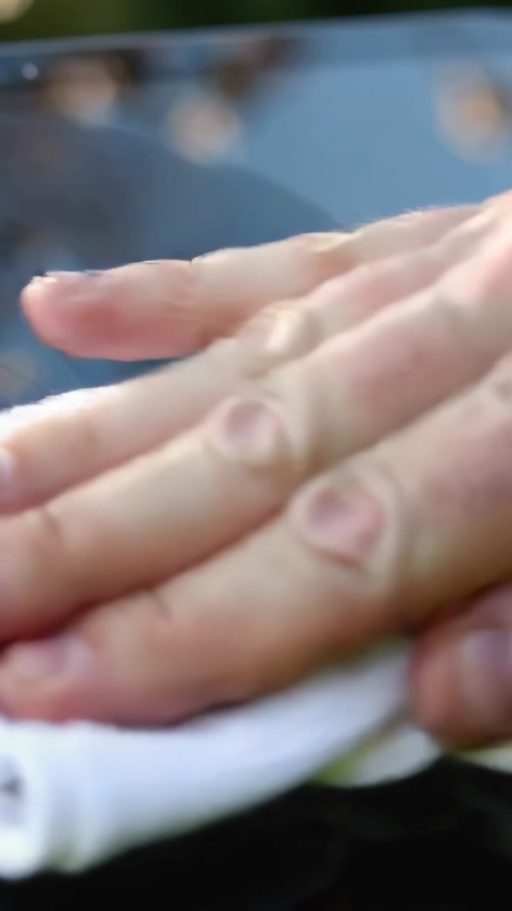 Vertical video: Placing white cloth, hands pressing and wiping dark car hood in driveway for shine