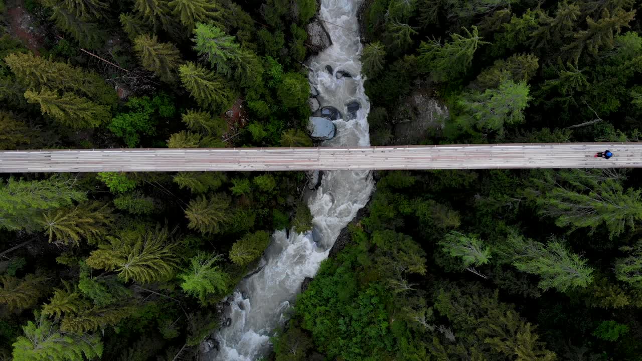 vista aérea de arriba hacia abajo de un excursionista que cruza un puente colgante en lo alto del valle del río ródano en valais, suiza en el puente goms