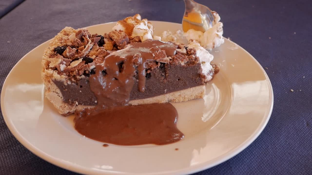 Static view of a tea spoon taking a piece of chocolate cheese cake with cream and chocolate sauce