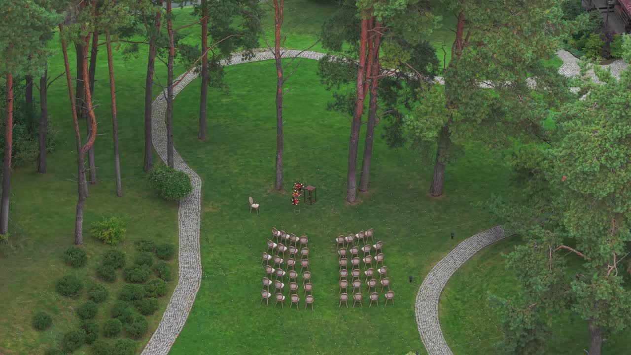 Aerial shot of an intimate wedding ceremony setup in a serene forest with chairs arranged in rows among tall trees and winding stone paths