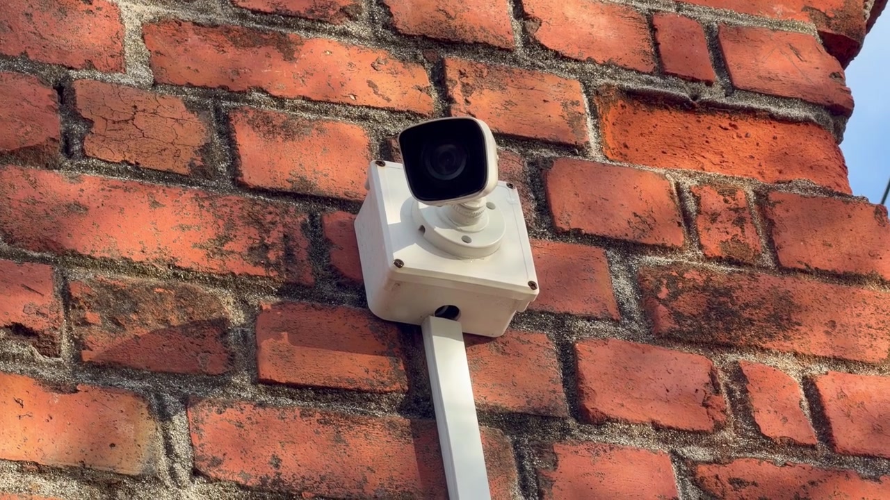 A modern CCTV surveillance camera mounted on a weathered red brick wall, symbolizing security, monitoring, and urban safety. Ideal for footage related to home security, business protection, privacy.