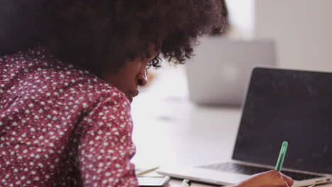 Millennial-black-businesswoman-sitting-at-a-table-in-an-office-making-notes,-close-up