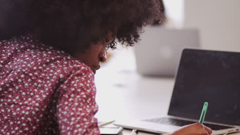 mujer de negocios negra del milenio sentada en una mesa en una oficina tomando notas, de cerca
