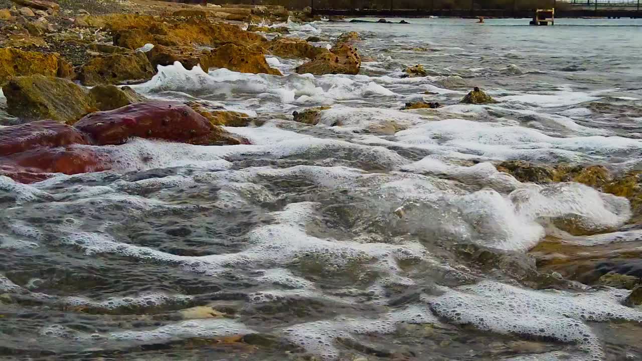 mirando el agua tranquila convirtiéndose en olas golpeando las rocas en el camino a la orilla