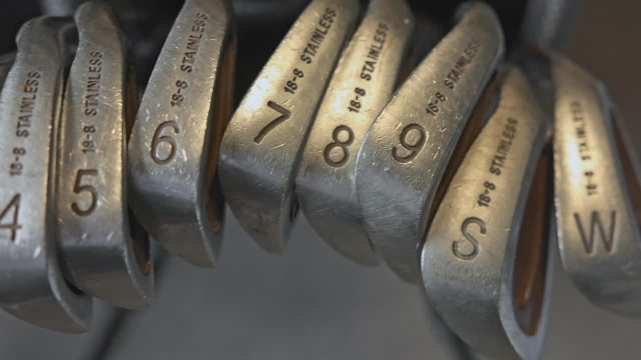 slow panning shot of a golf bag complete with various irons and wedges