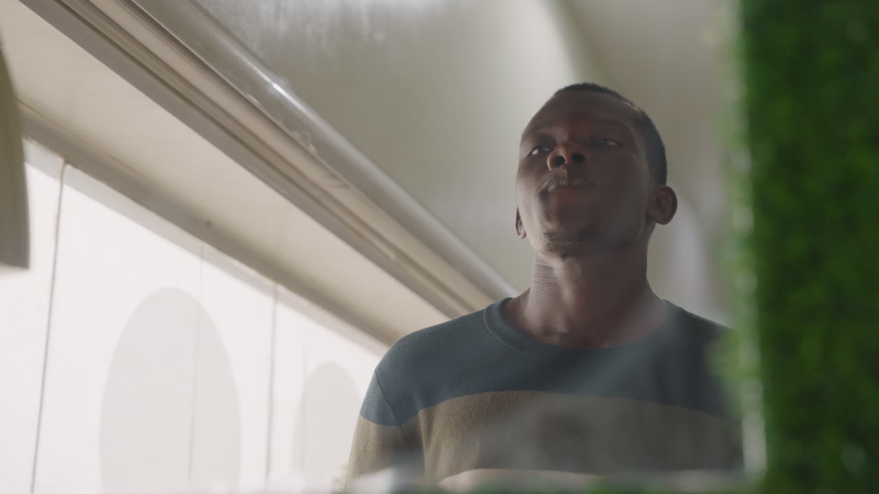 Black man staring through window glass, late night after date, reflective expression, apartment light casting shadow, distant gaze, subtle breath, thinking about relationship, contemplative mood, film