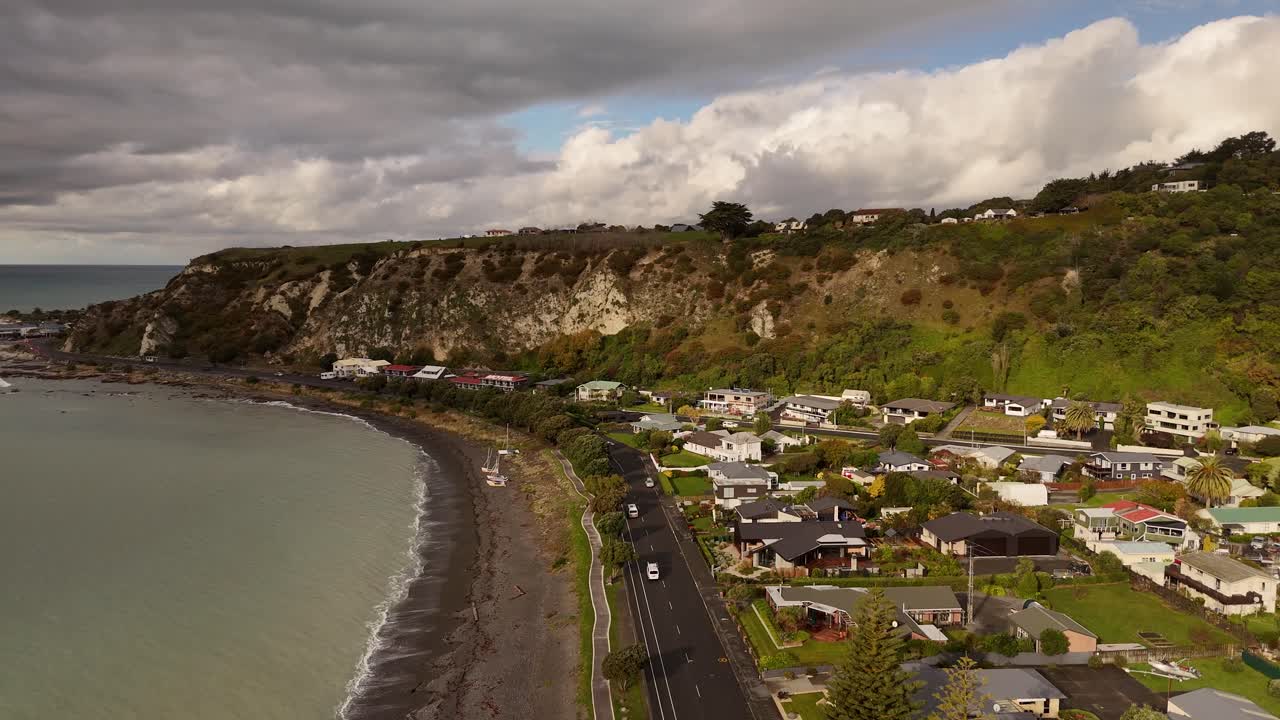 Aerial drone flying up over Kaikoura coastline, dark sand beach, cliffs, houses, South Island, New Zealand