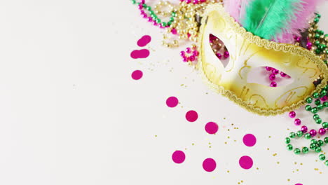 video of masquerade mask, mardi gras beads and confetti on white background with copy space