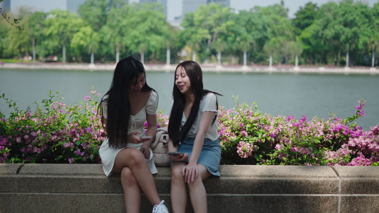 เพื่อนผู้หญิงเอเชียรุ่นใหม่มีความสุขกับการพูดคุยกันริมทะเลสาบในสวนสาธารณะ