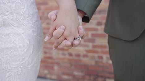 newly married couple holding hands with big wedding ring and brick in background in 4k slow motion