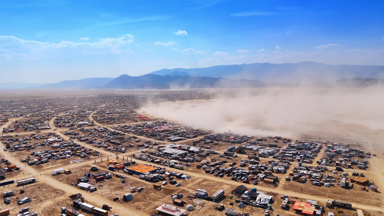 Grande pennacchio di polvere su un insediamento temporaneo nel deserto, vista aerea. Prospettiva aerea di una nuvola di polvere sollevata dal vento che si muove attraverso una città-accampamento temporanea in una secca valle di montagna.