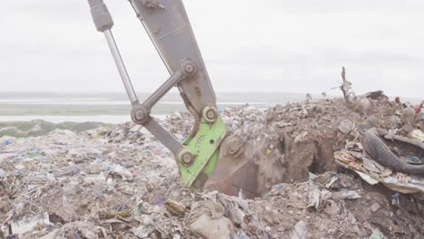 Digger-clearing-rubbish-piled-on-a-landfill-full-of-trash-